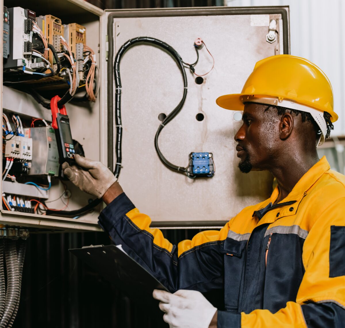 Engineer in a yellow hard hat testing an electrical control panel
